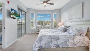 Een slaapkamer met een bed, een plafondventilator, een televisie, een raam met jaloezieën en een deur naar een balkon.