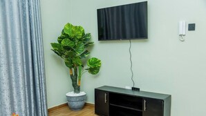 Et værelse med et fladskærms-tv på væggen, et sort møbelarrangement under det, og en stor potteplante til venstre.