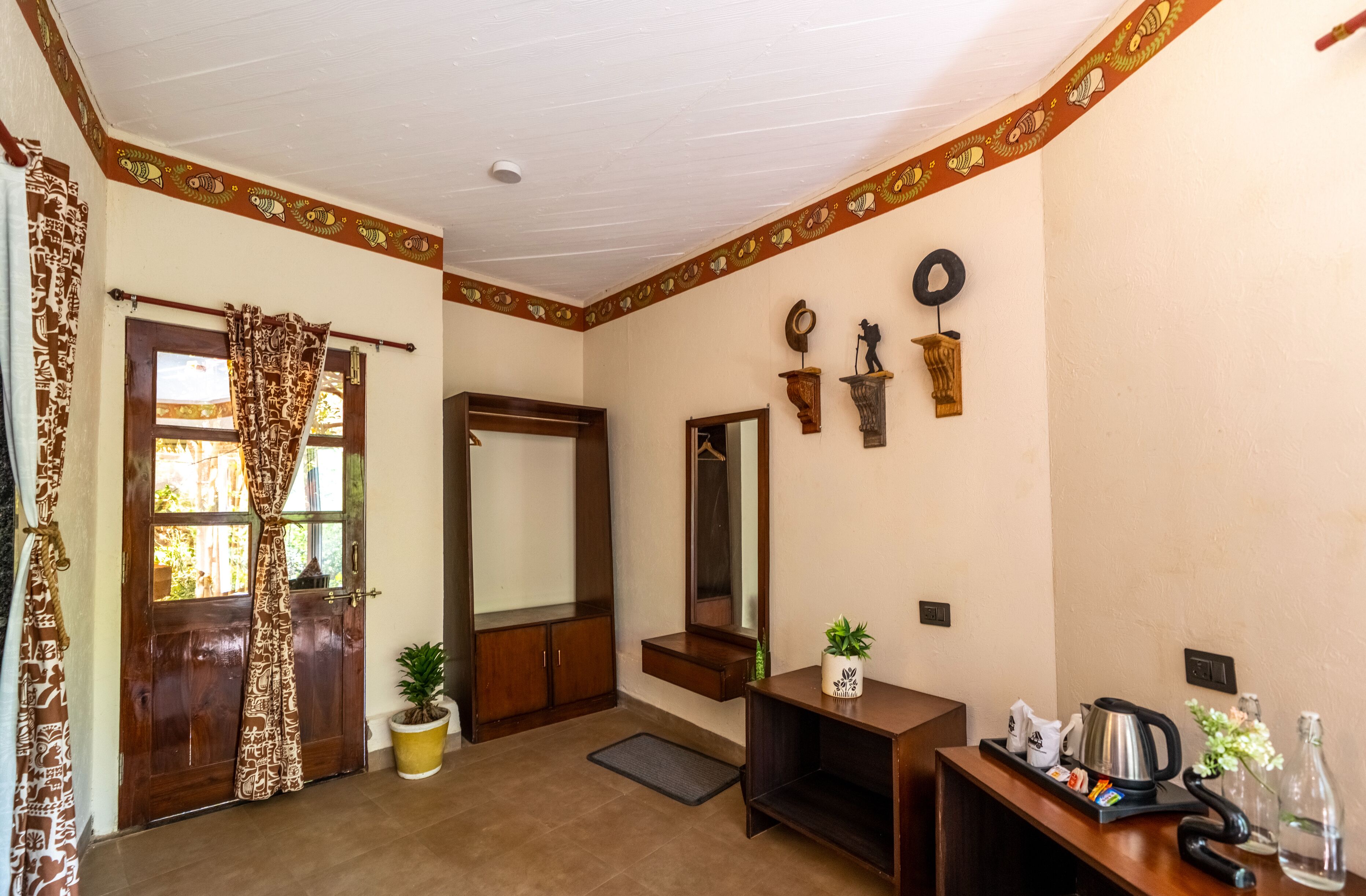 Una habitación con puerta de madera, un espejo, una mesita con una planta y una estantería con adornos.