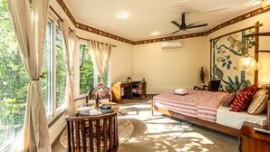 A bedroom with a bed, desk, chair, and a view of greenery outside. - Jungle Ghar  (Pipariya)