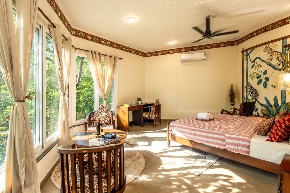 A bedroom with a bed, desk, chair, and a view of greenery outside.