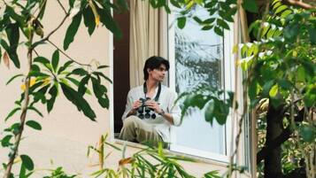 Eine Person sitzt an einem Fenster, umgeben von Pflanzen.