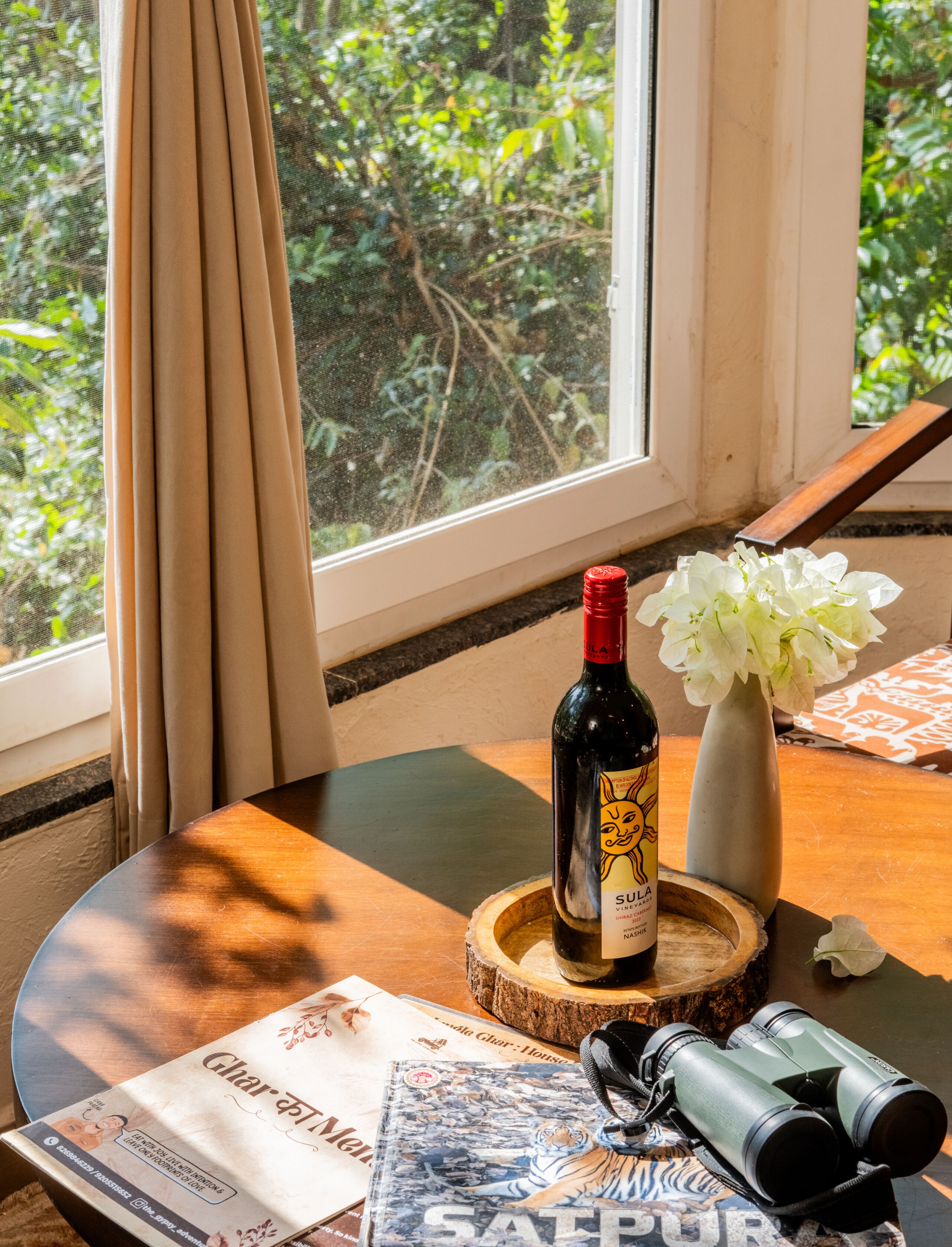 A table with a bottle of wine, a vase with flowers, binoculars, and a magazine.