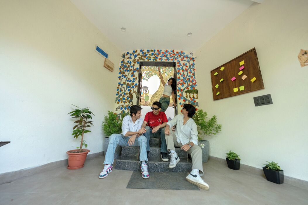 A group of people sitting on steps in a room with a decorative wall and potted plants.