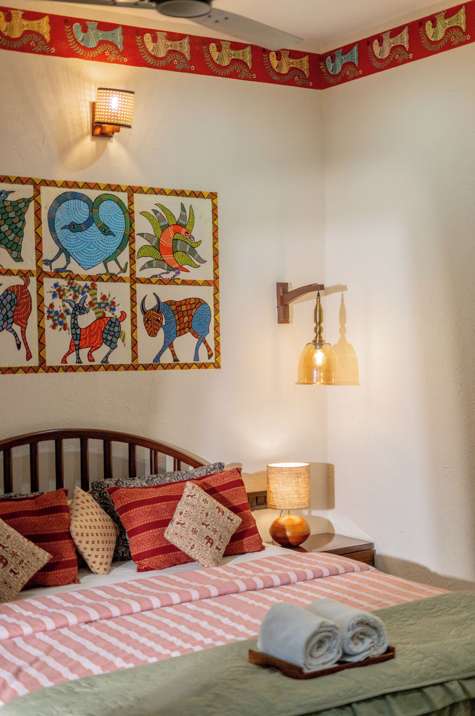 Una cama bien hecha con almohadas estampadas, una pared con arte temático de animales y una lámpara fijada a la pared.