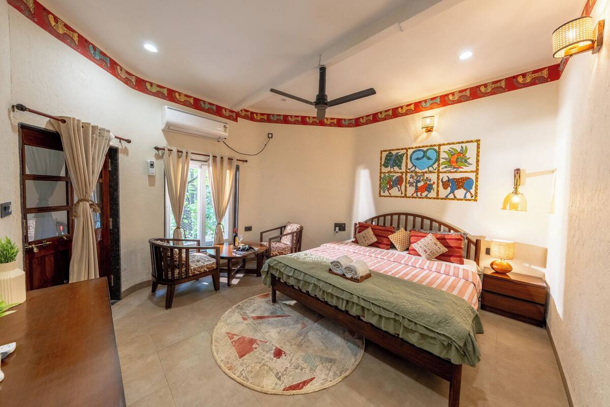 A bedroom with a bed, bedside table, lamp, chair, and a small table with a plant.