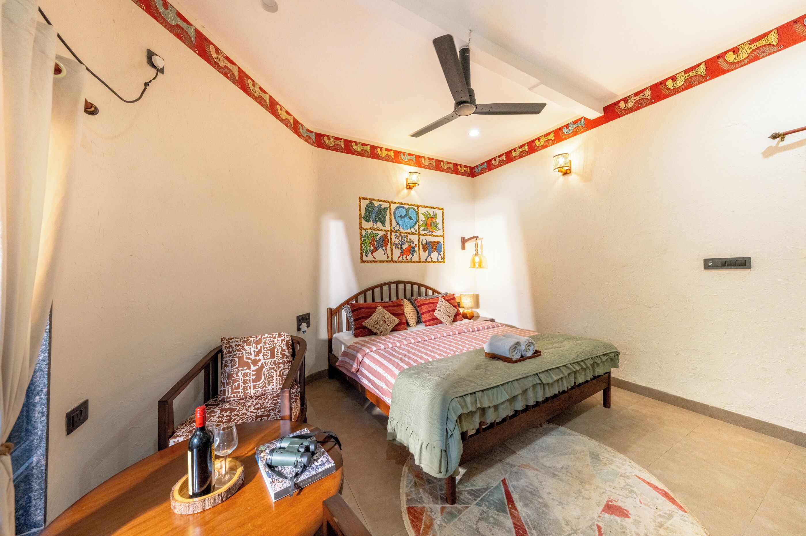 Ein Schlafzimmer mit einem Bett, einem Schreibtisch mit Flasche und Gläsern, einem Deckenventilator und einer Wand mit dekorativer Beleuchtung.
