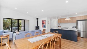 A modern kitchen with a central island, a dining area with a wooden table and chairs, and a living area with a sofa and a fireplace. - Tranquil at Rosedale (Rosedale)