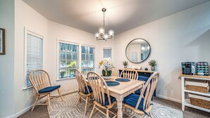 Un coin repas avec une table en bois, des chaises rembourrées bleues, un lustre et une machine à café.