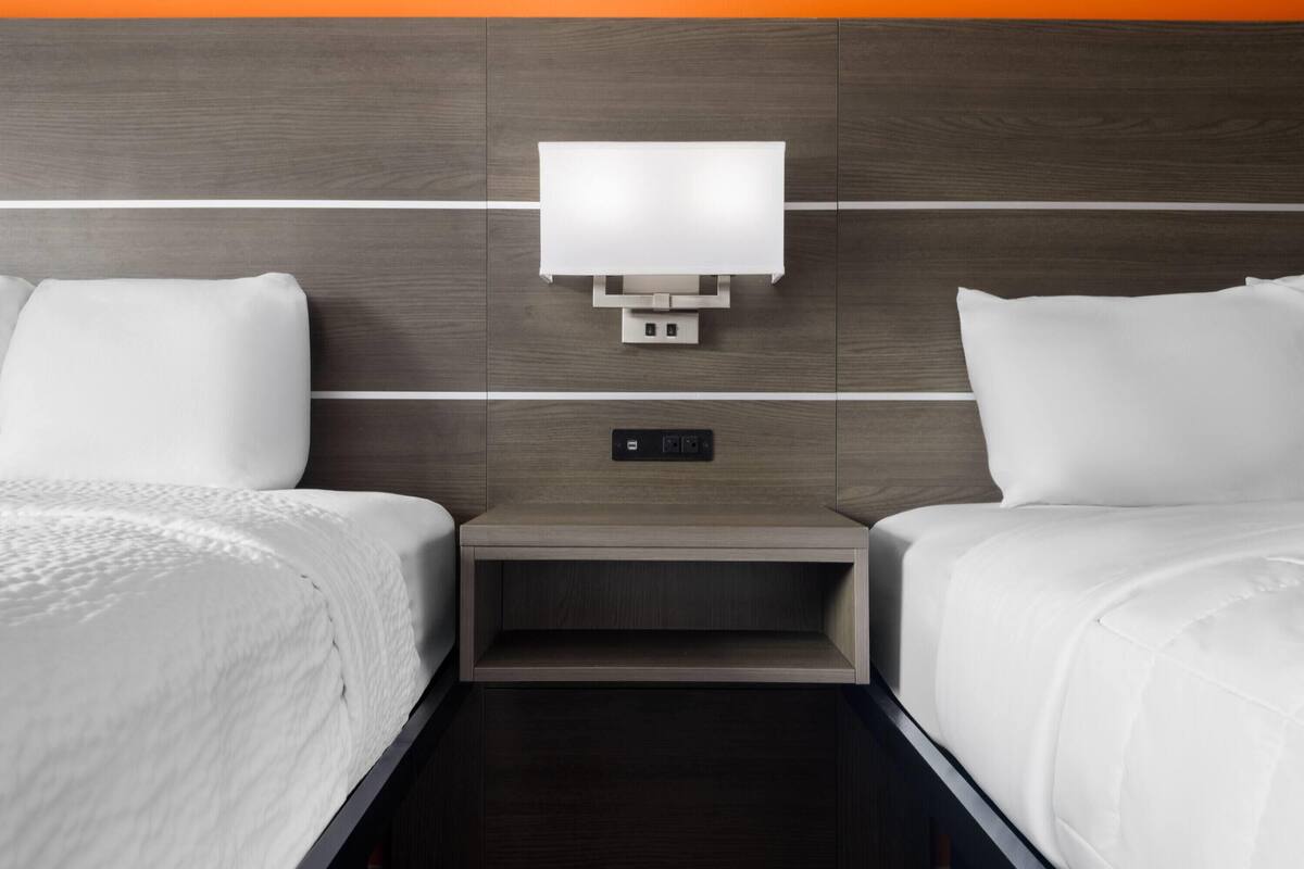 Een hotelkamer met twee bedden, een nachtkastje, een wandlamp en een stopcontact.