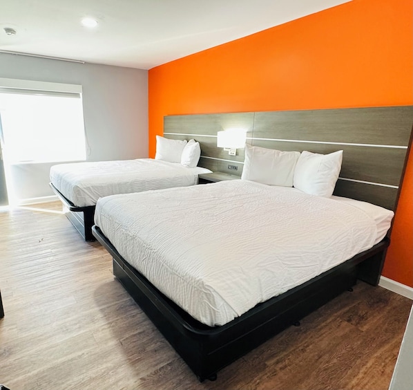Een hotelkamer met twee bedden, een houten vloer en een oranje accentmuur.