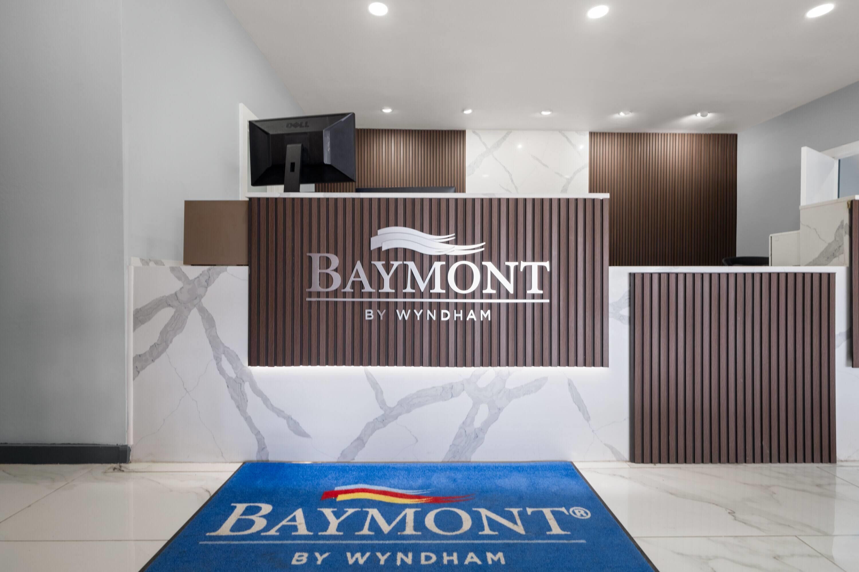 A reception area with a Baymont by Wyndham sign, a reception desk, and a blue carpet with the hotel logo.