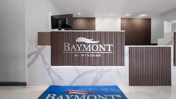 A reception area with a Baymont by Wyndham sign, a reception desk, and a blue carpet with the hotel logo.