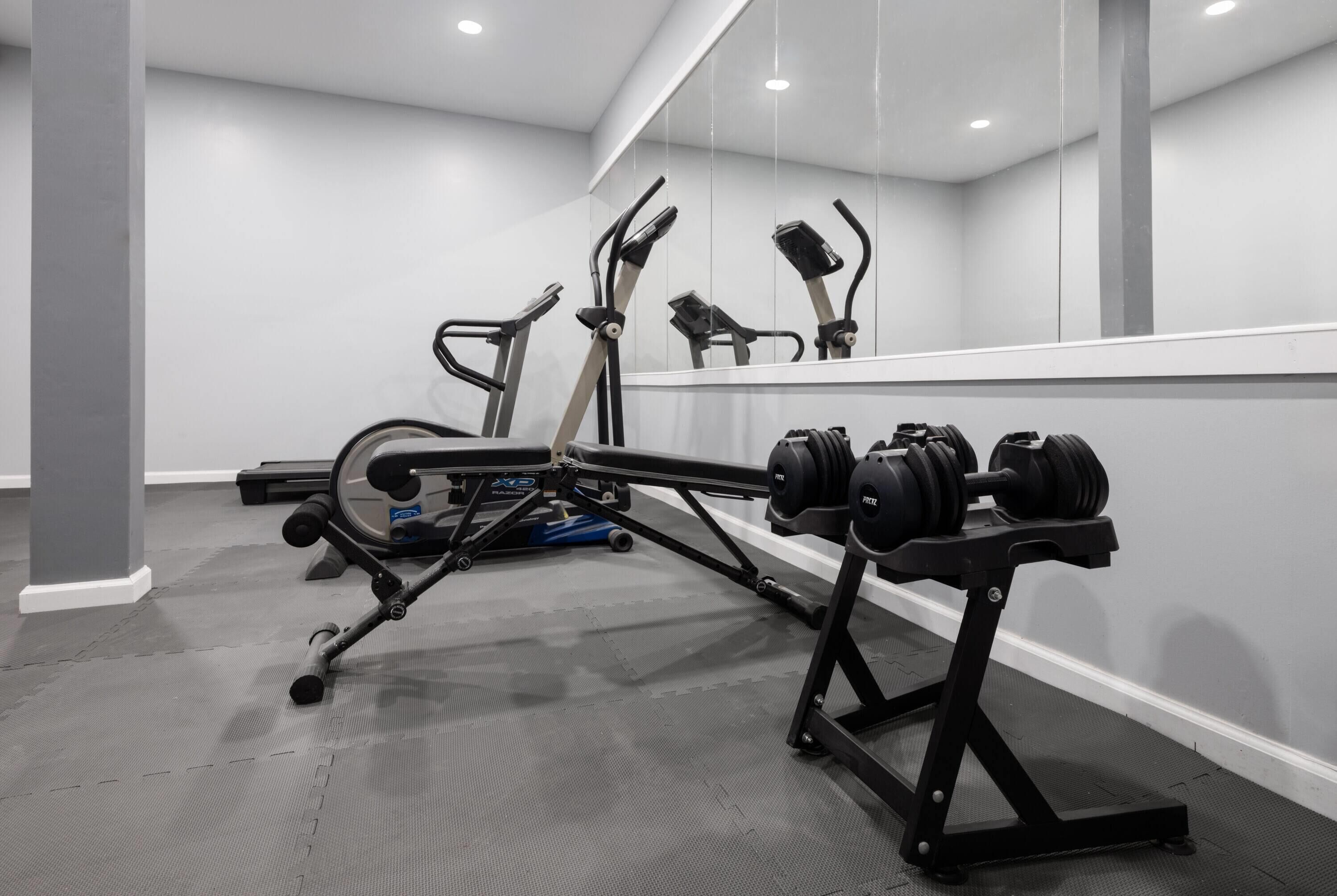 Uma academia com equipamentos de ginástica, incluindo esteira, banco de musculação e halteres.