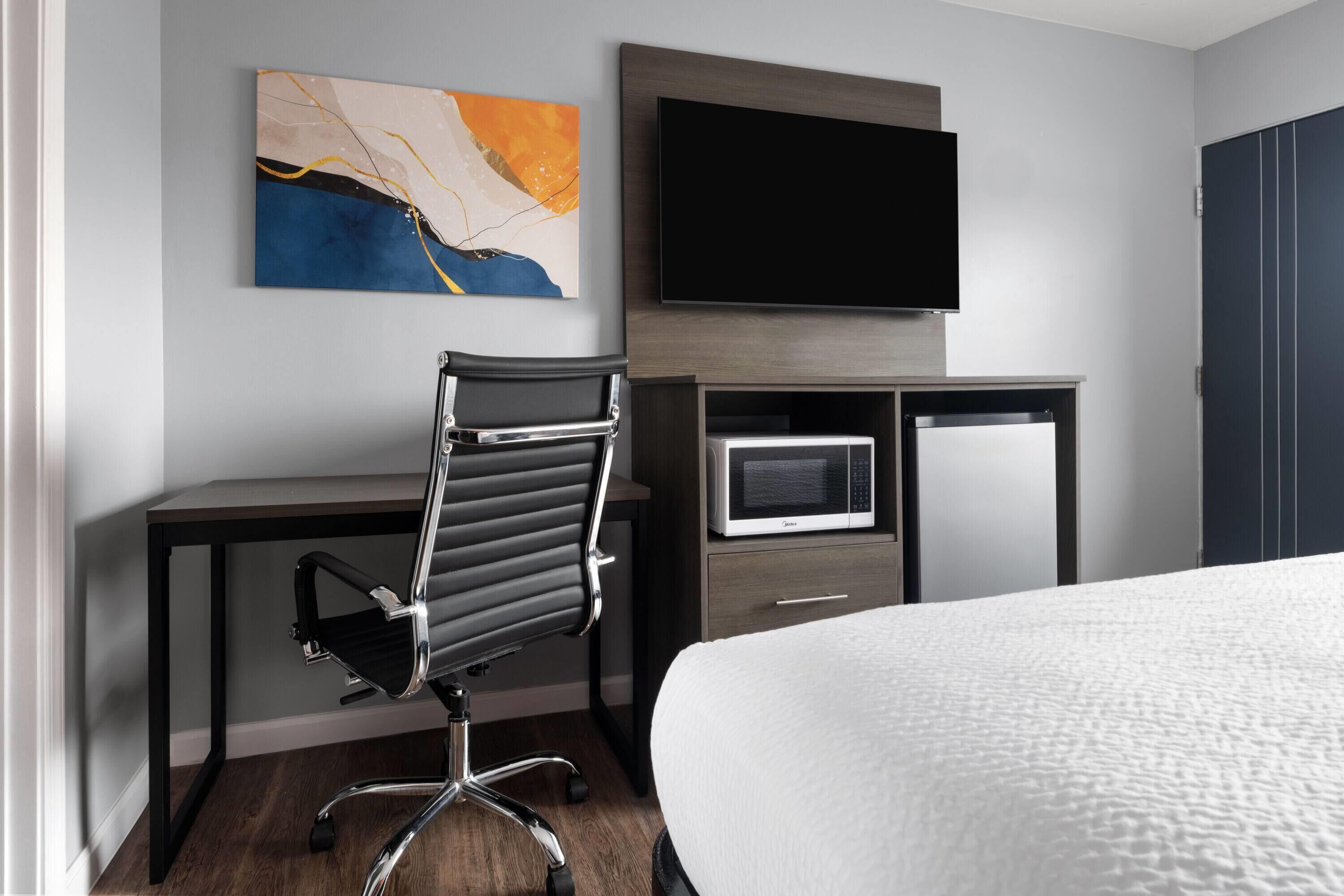 A hotel room with a bed, a desk with a chair, a flat-screen TV, a microwave, and a cabinet.