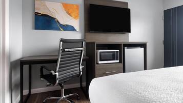 A hotel room with a bed, a desk with a chair, a flat-screen TV, a microwave, and a cabinet.
