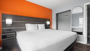 Een moderne hotelkamer met een groot bed, twee nachtkastjes, een spiegel en een oranje accentmuur.