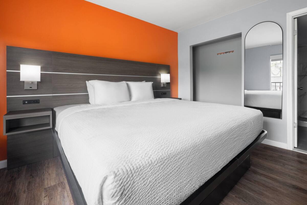 Een moderne hotelkamer met een groot bed, twee nachtkastjes, een spiegel en een oranje accentmuur.