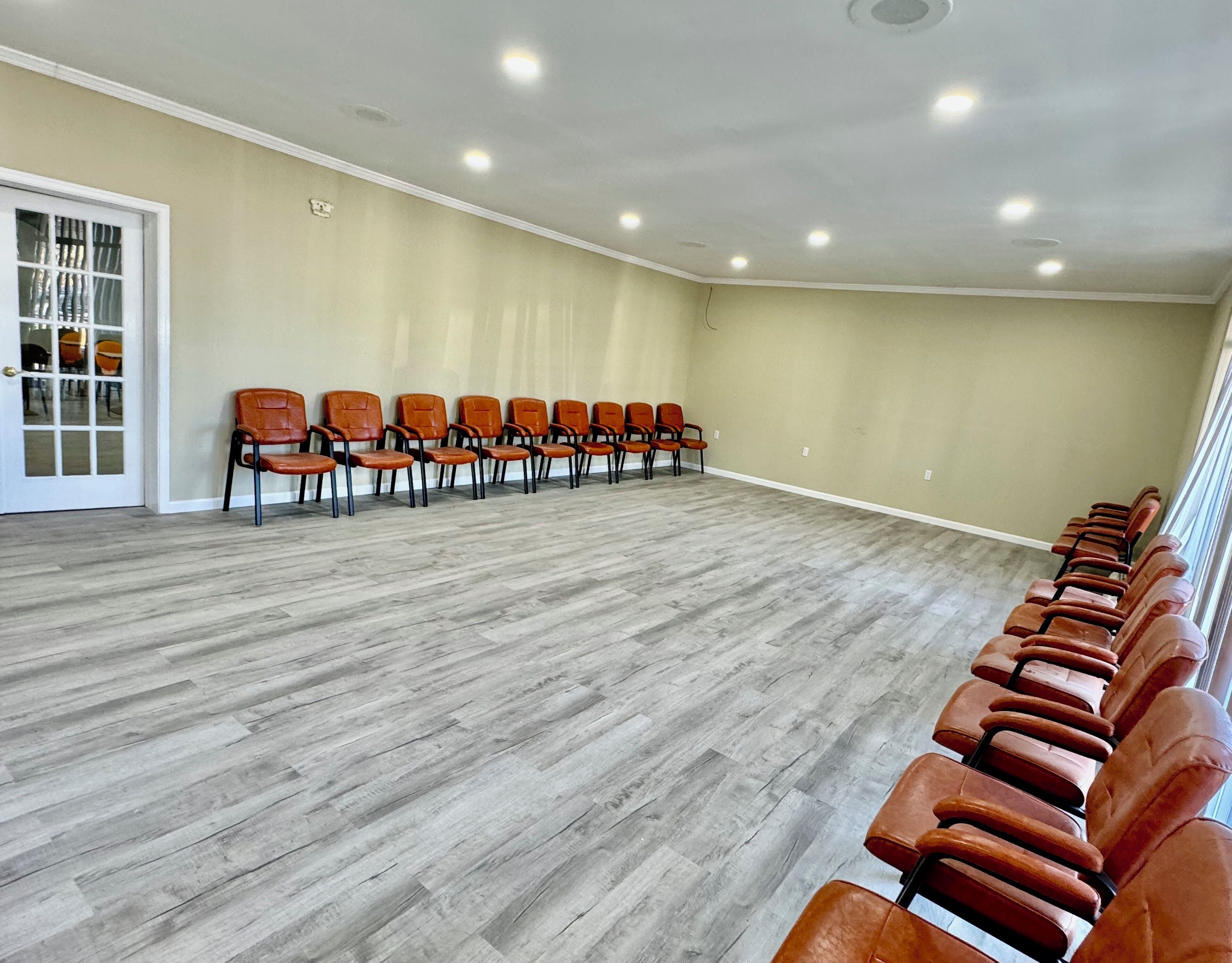 A conference room with rows of chairs, a wooden floor, and a beige wall.