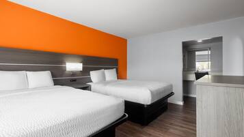 A hotel room with two beds, a wooden headboard, a small desk, and a bathroom visible through an open door.