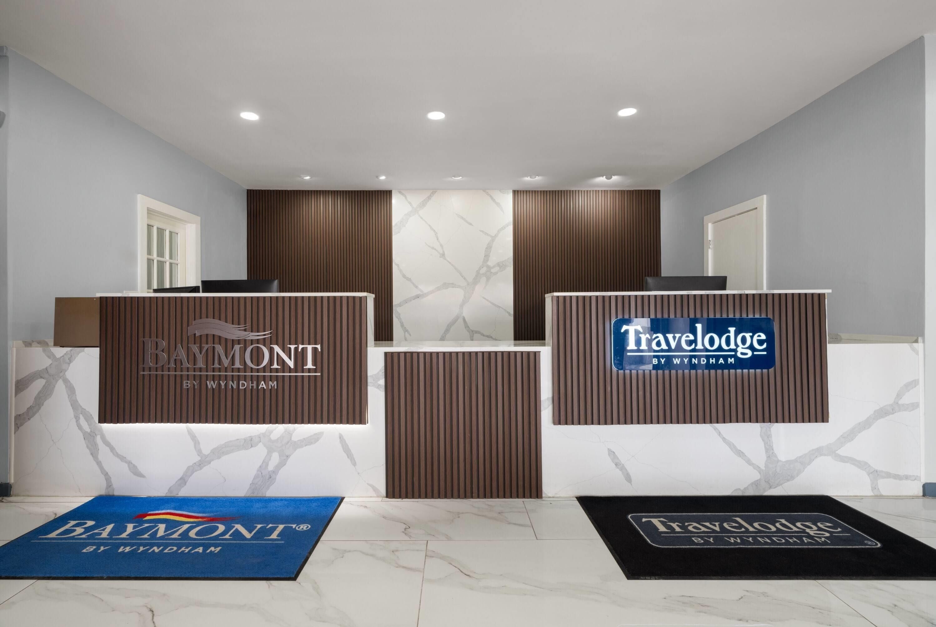 A reception area with two counters labeled 'Baymont by Wyndham' and 'Travelodge by Wyndham'.