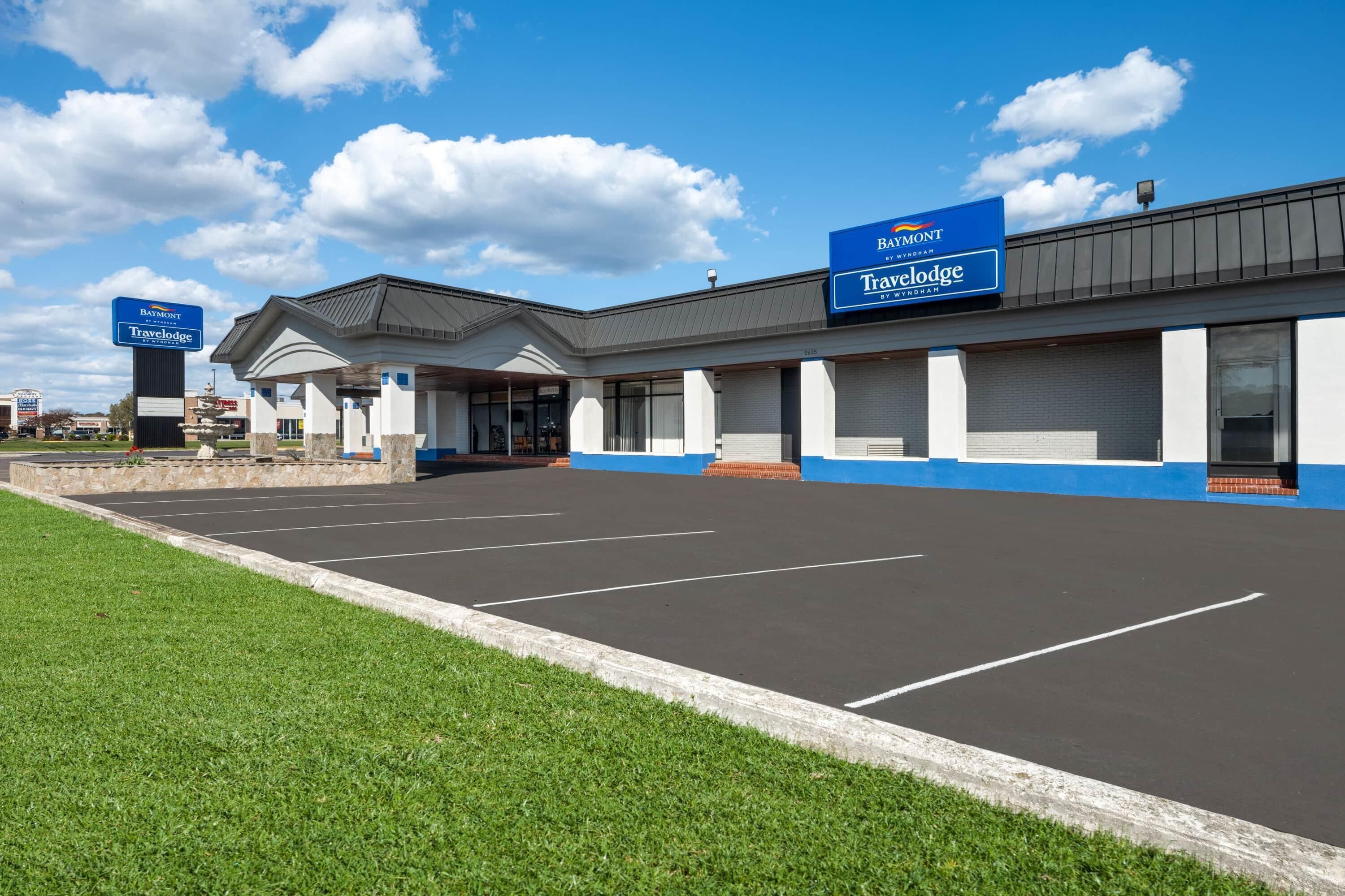 A travel lodge with a large parking lot, a covered entrance, and signage for the Baymont Travelodge.