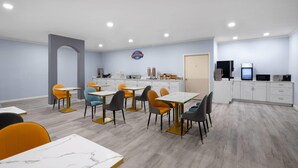 Een moderne eethoek met meerdere tafels en stoelen, een keuken op de achtergrond en een bordje dat een ontbijthoek aangeeft.