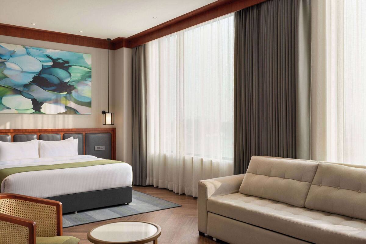 A hotel room with a large bed, a sofa, a chair, and a painting on the wall.