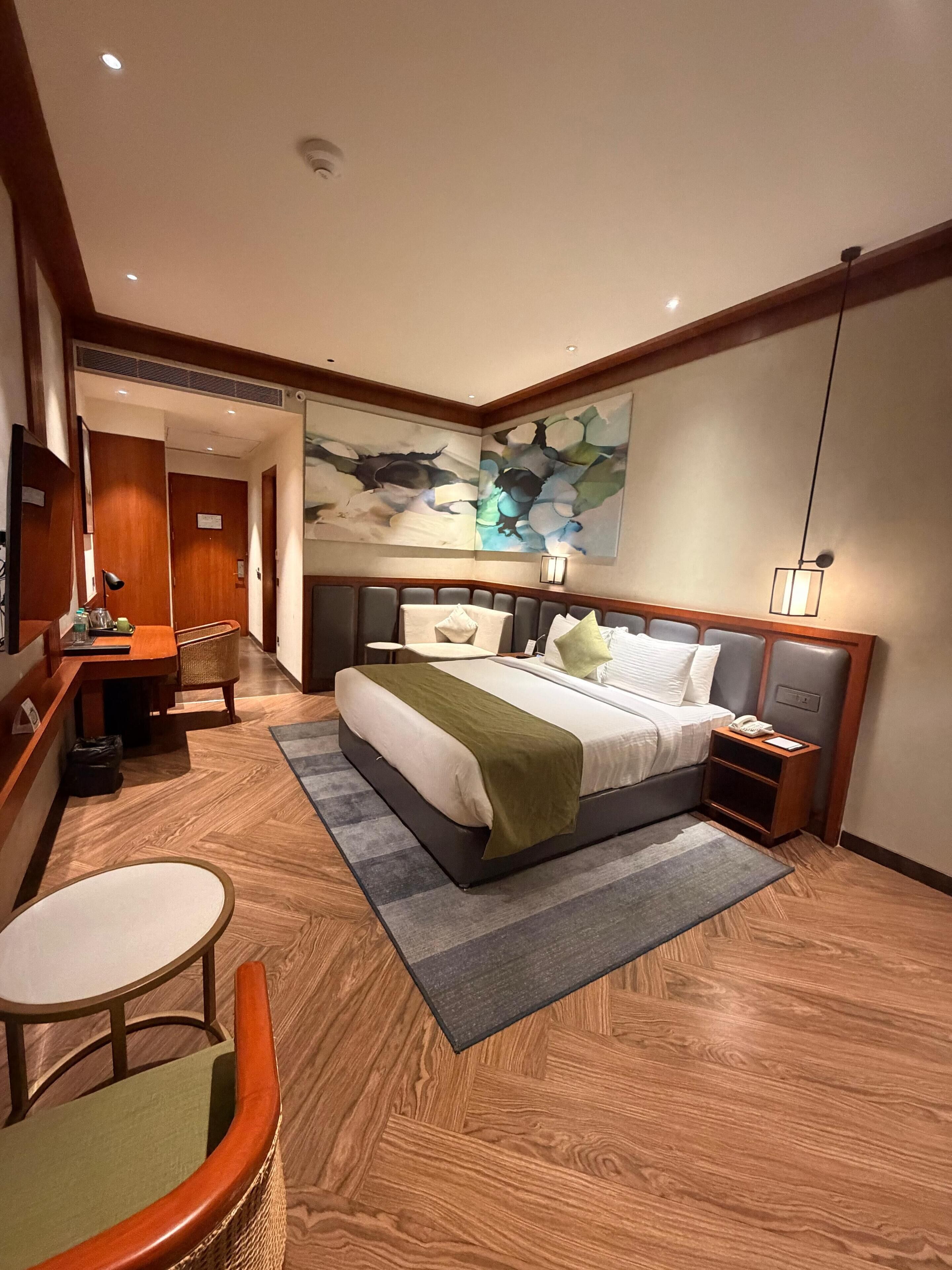 A hotel room with a bed, bedside table, lamp, and a view of the hallway.