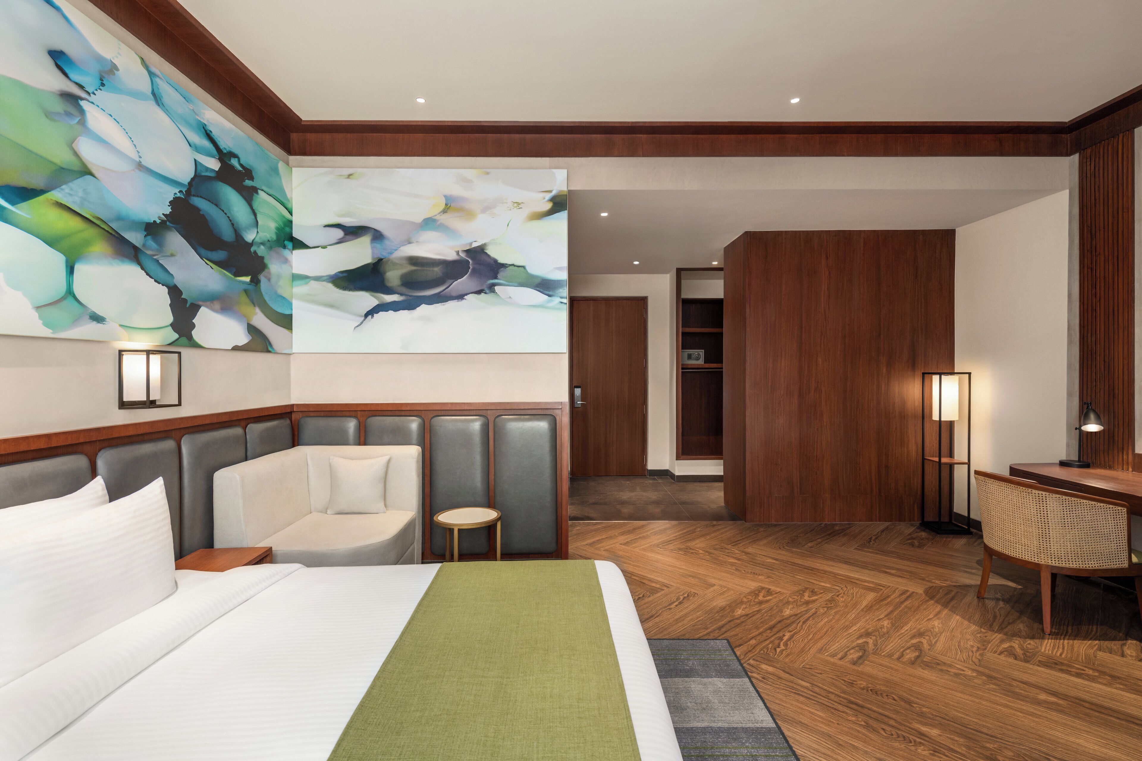 A hotel room with a large bed, a seating area with a small table, a desk with a chair, and a large abstract painting on the wall.