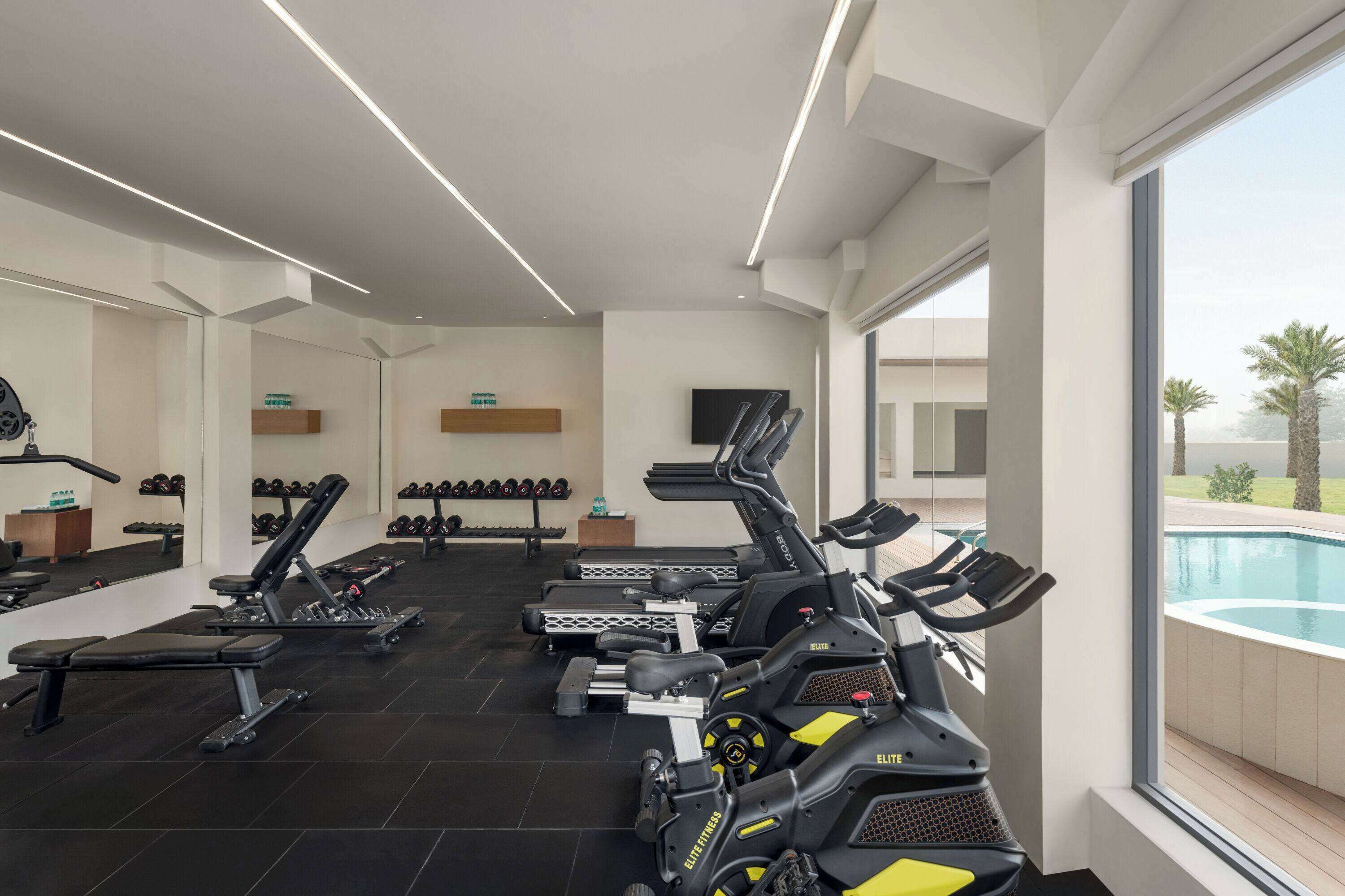 Ein modernes Fitnessstudio mit unterschiedlichen Trainingsgeräten, einem durch große Fenster einsehbaren Pool und einem klaren, minimalistischen Design.