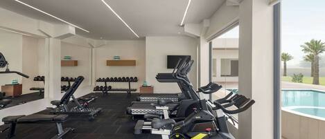 Ein modernes Fitnessstudio mit unterschiedlichen Trainingsgeräten, einem durch große Fenster einsehbaren Pool und einem klaren, minimalistischen Design.