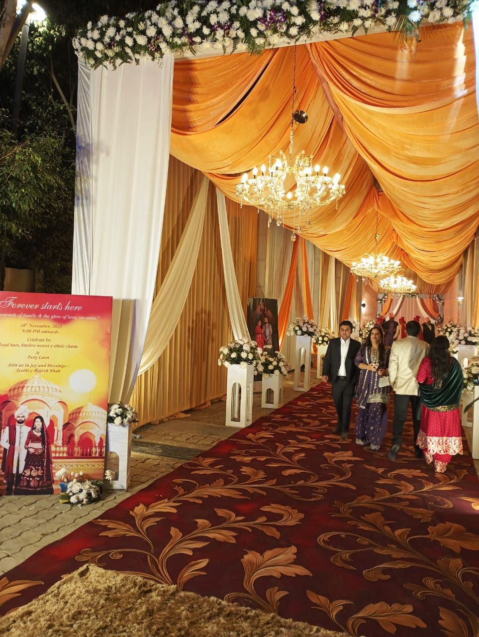A decorated event space with draped curtains, chandeliers, and floral arrangements.