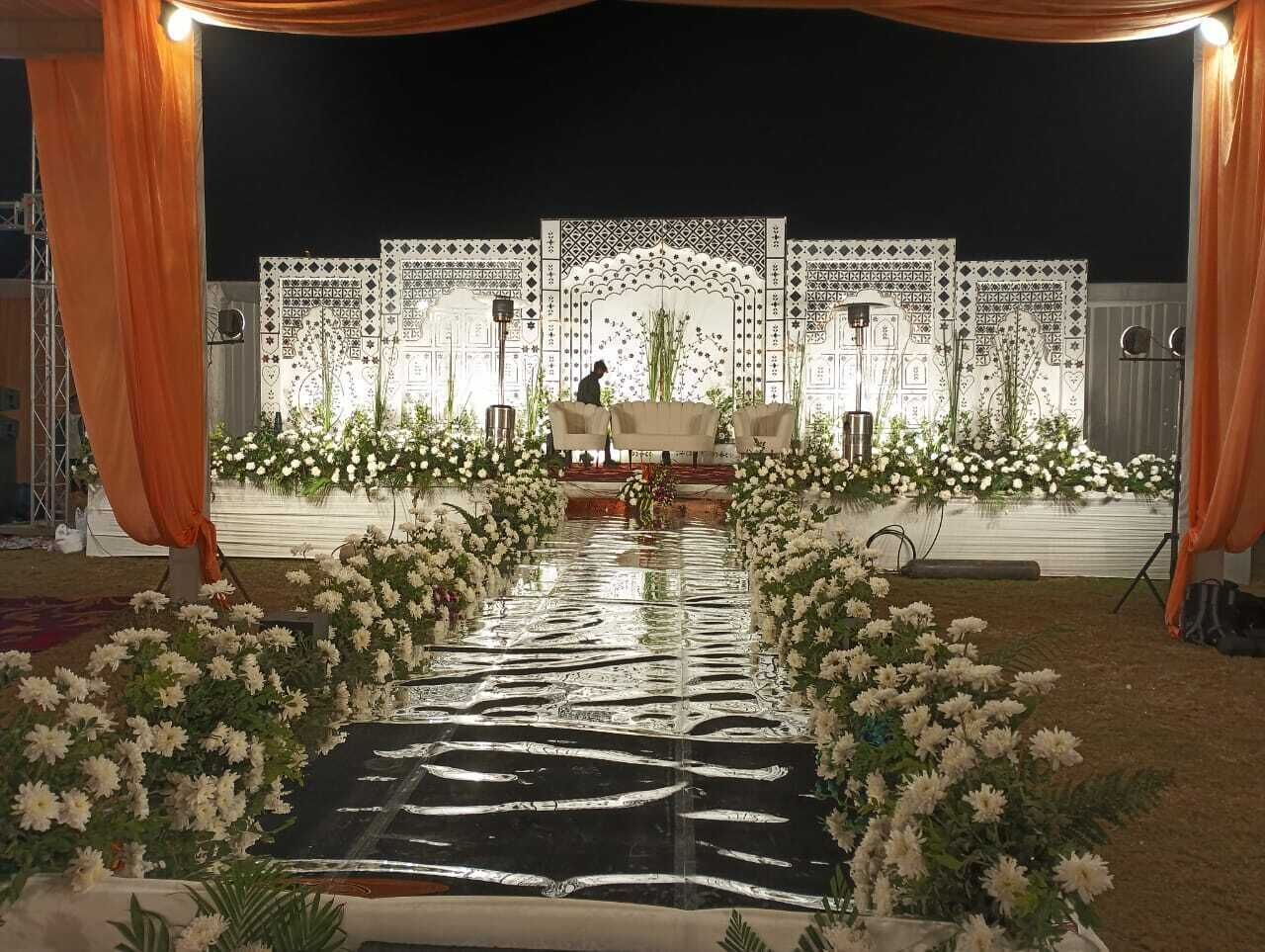 Un escenario con una decoración floral y un atril, rodeado de telas drapeadas y un suelo reflectante.