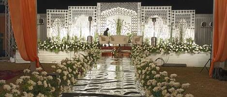 Un escenario con una decoración floral y un atril, rodeado de telas drapeadas y un suelo reflectante.