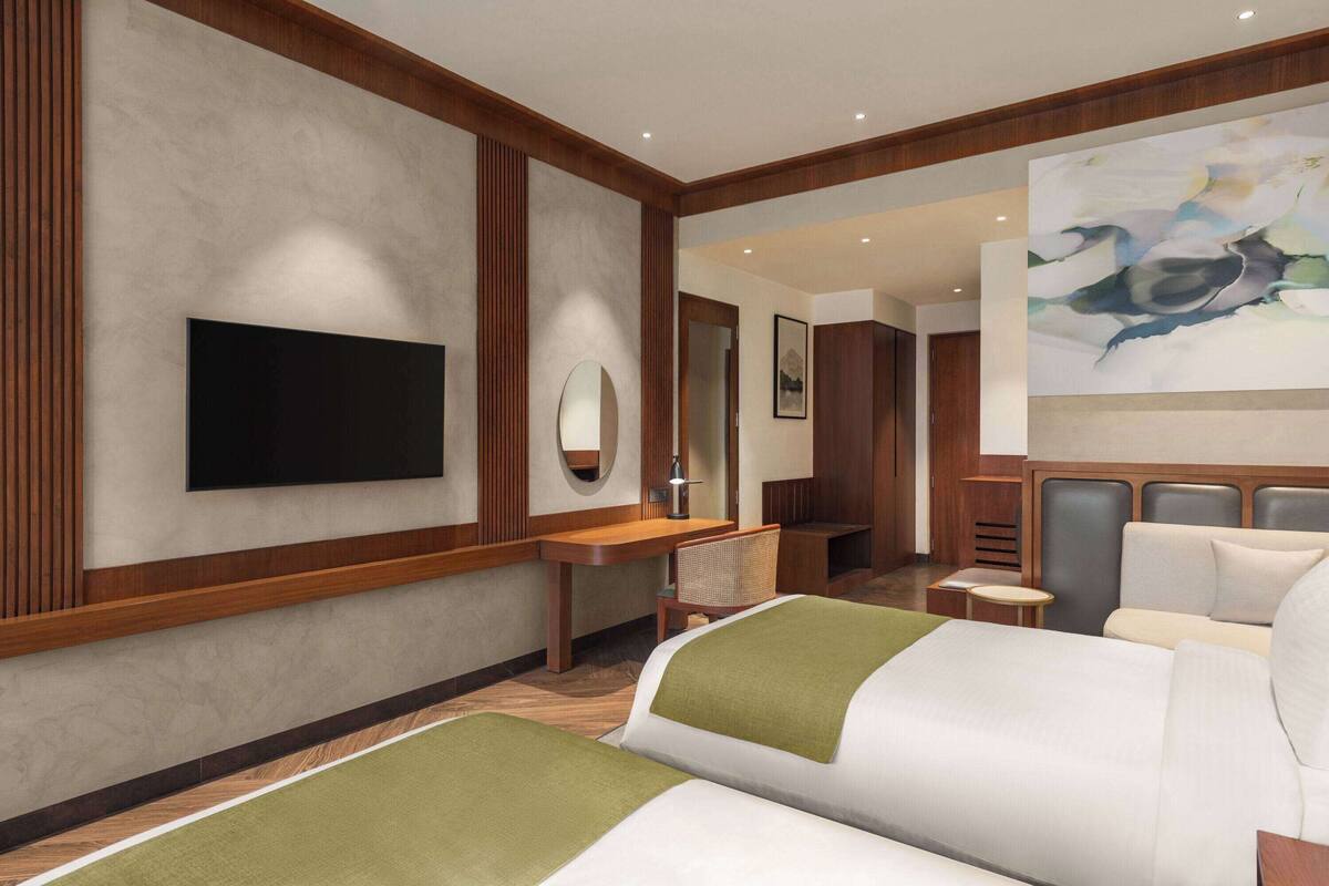 A hotel room with a large bed, a desk, a chair, a television, and a painting on the wall.