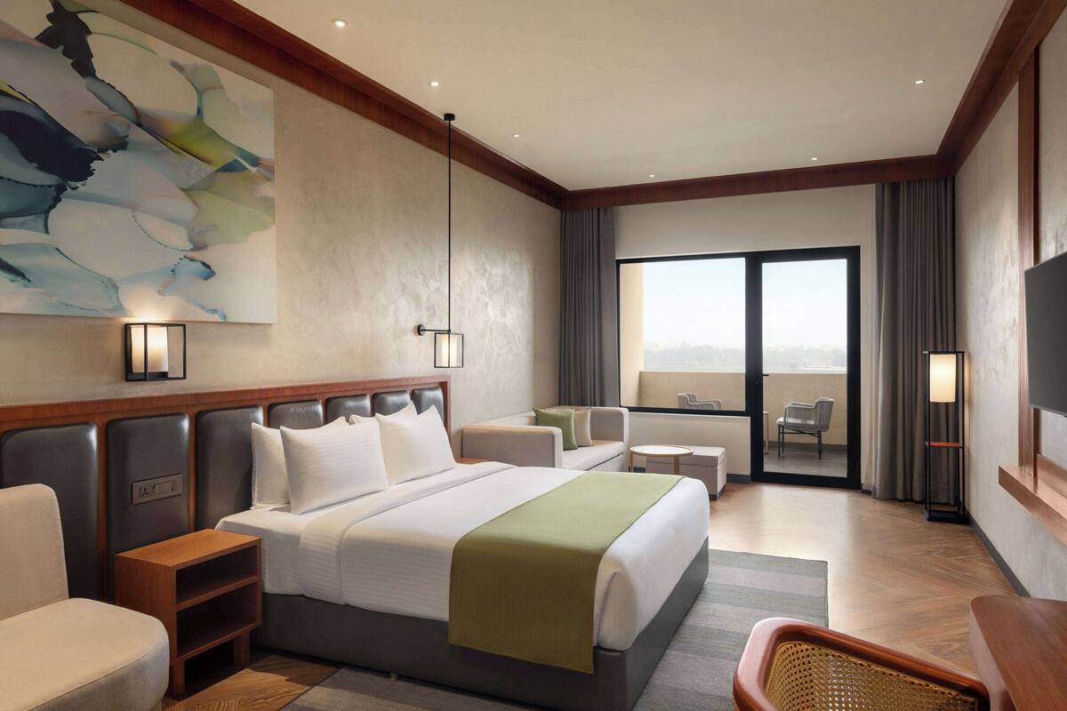 A hotel room with a large bed, a seating area with a sofa and chairs, a small table, and a large window offering a view.