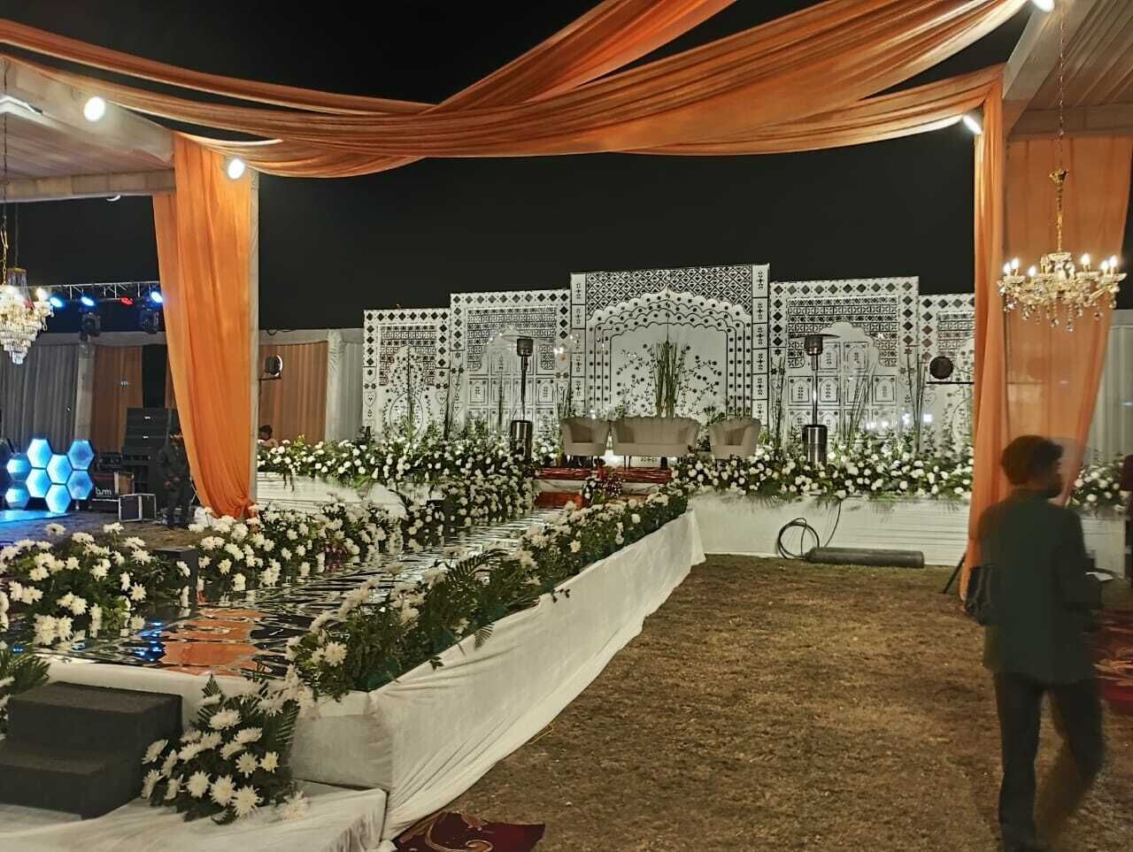 Un espacio para eventos al aire libre con escenario, arreglos florales y una estructura tipo carpa.