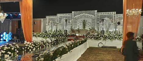 Un espacio para eventos al aire libre con escenario, arreglos florales y una estructura tipo carpa.