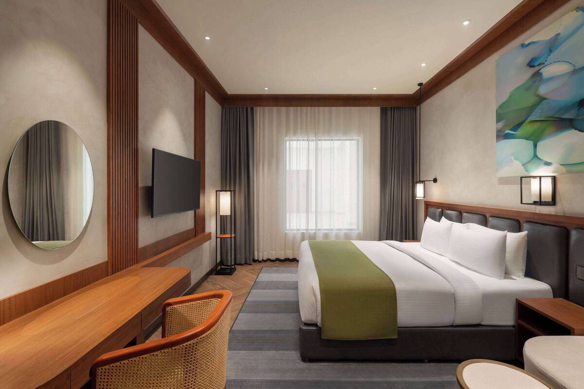 A hotel room with a large bed, a desk, a chair, a television, and a painting on the wall.