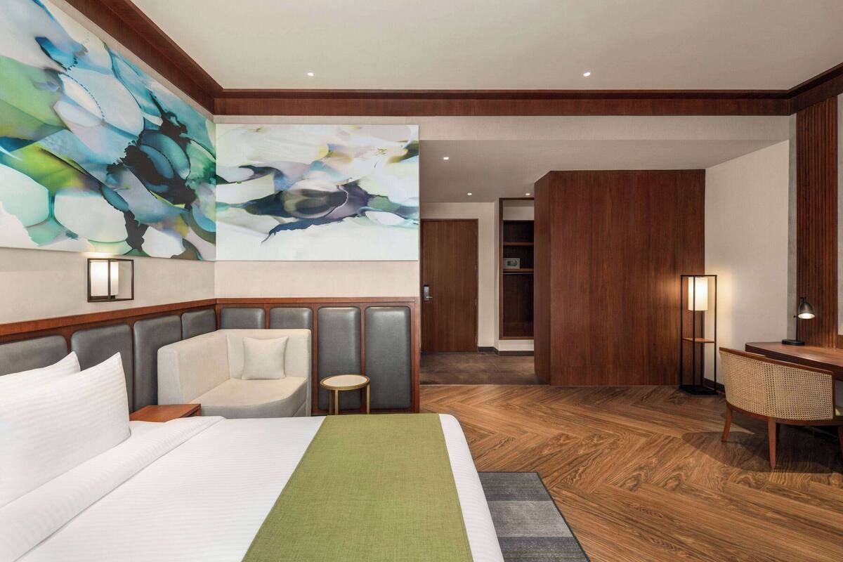 A hotel room with a large bed, a seating area, a desk, and a large abstract painting on the wall.