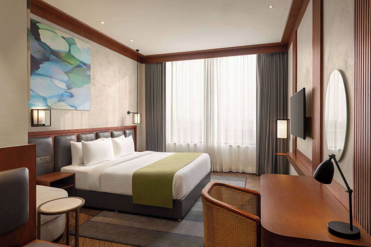 A hotel room with a large bed, a desk, a chair, a television, and a painting on the wall.