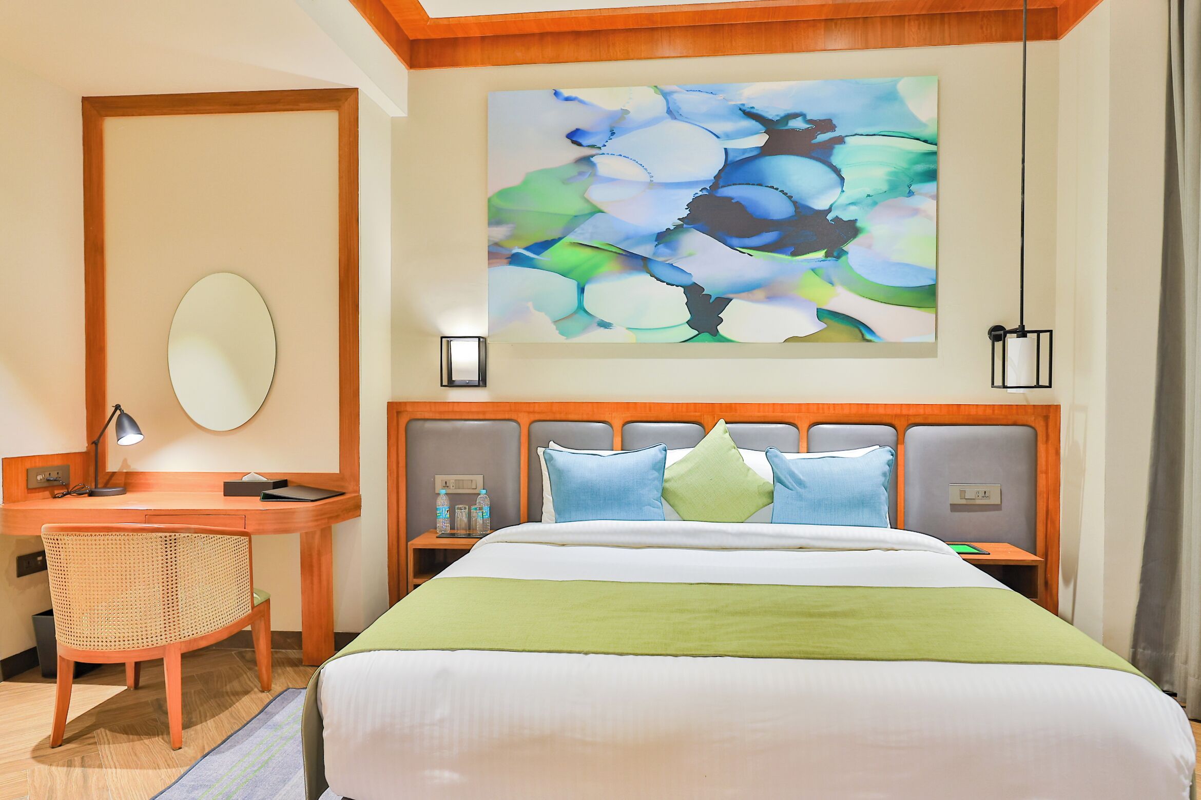 A hotel room with a bed, desk, chair, and artwork on the wall.