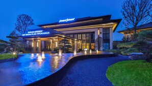 A hotel with a modern facade, a well-lit entrance, and a water feature in front.