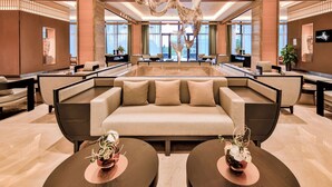 A spacious lobby with a large sofa, two round tables with vases, and a unique ceiling sculpture.