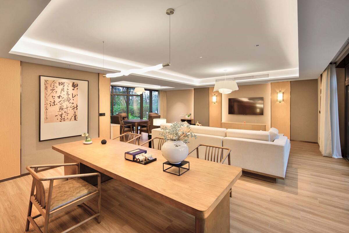 Une chambre d’hôtel moderne avec une table à manger en bois, un canapé et un téléviseur fixé au mur.
