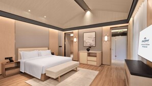 A modern hotel room with a large bed, bedside tables, a bench, a desk, and a TV.