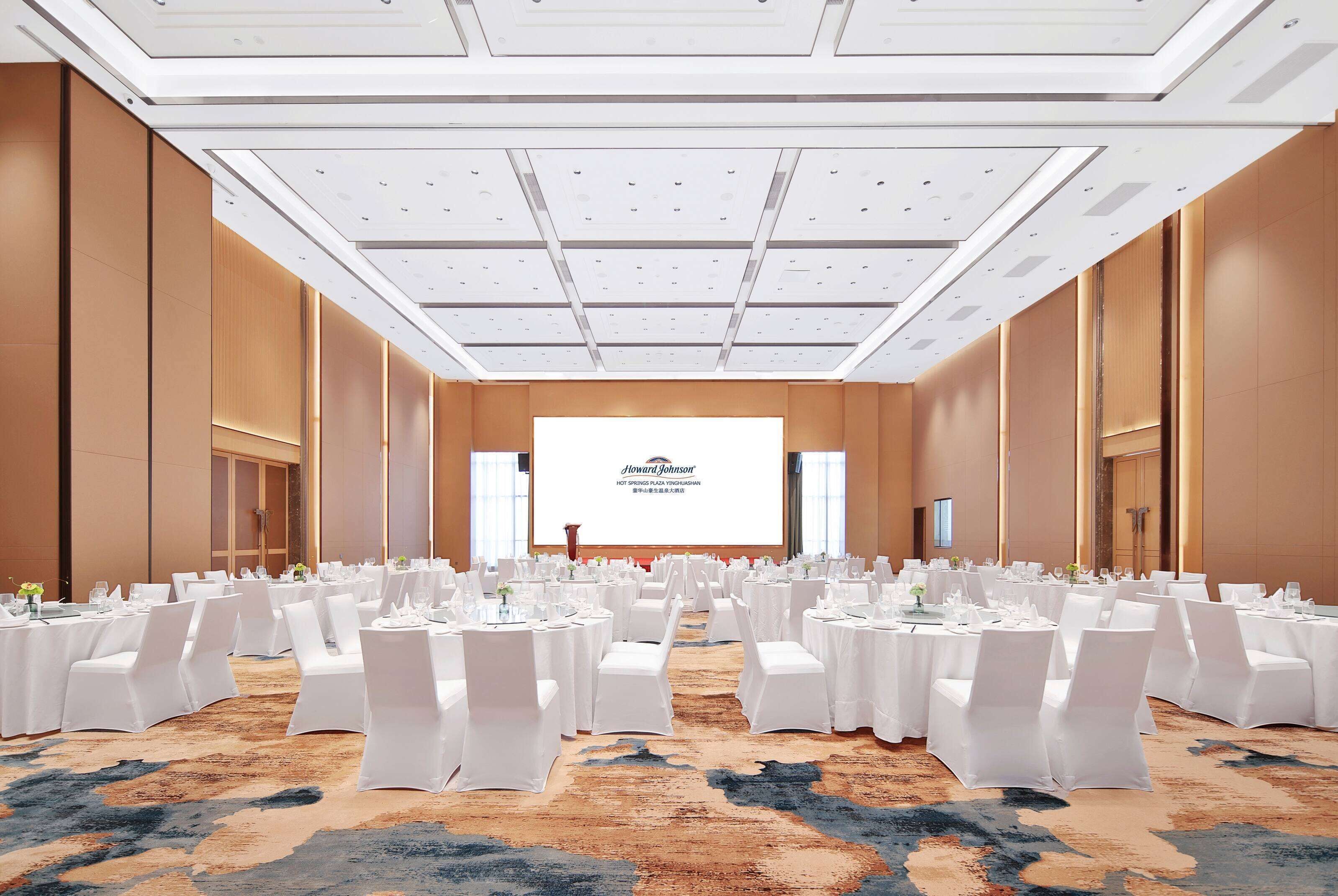 A conference room with round tables, white chairs, and a large screen at the front.