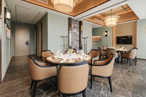 A dining area with round tables set for six, each with a white tablecloth, surrounded by beige upholstered chairs. - Howard Johnson Hot Springs Plaza Yinghuashan (Deyang)