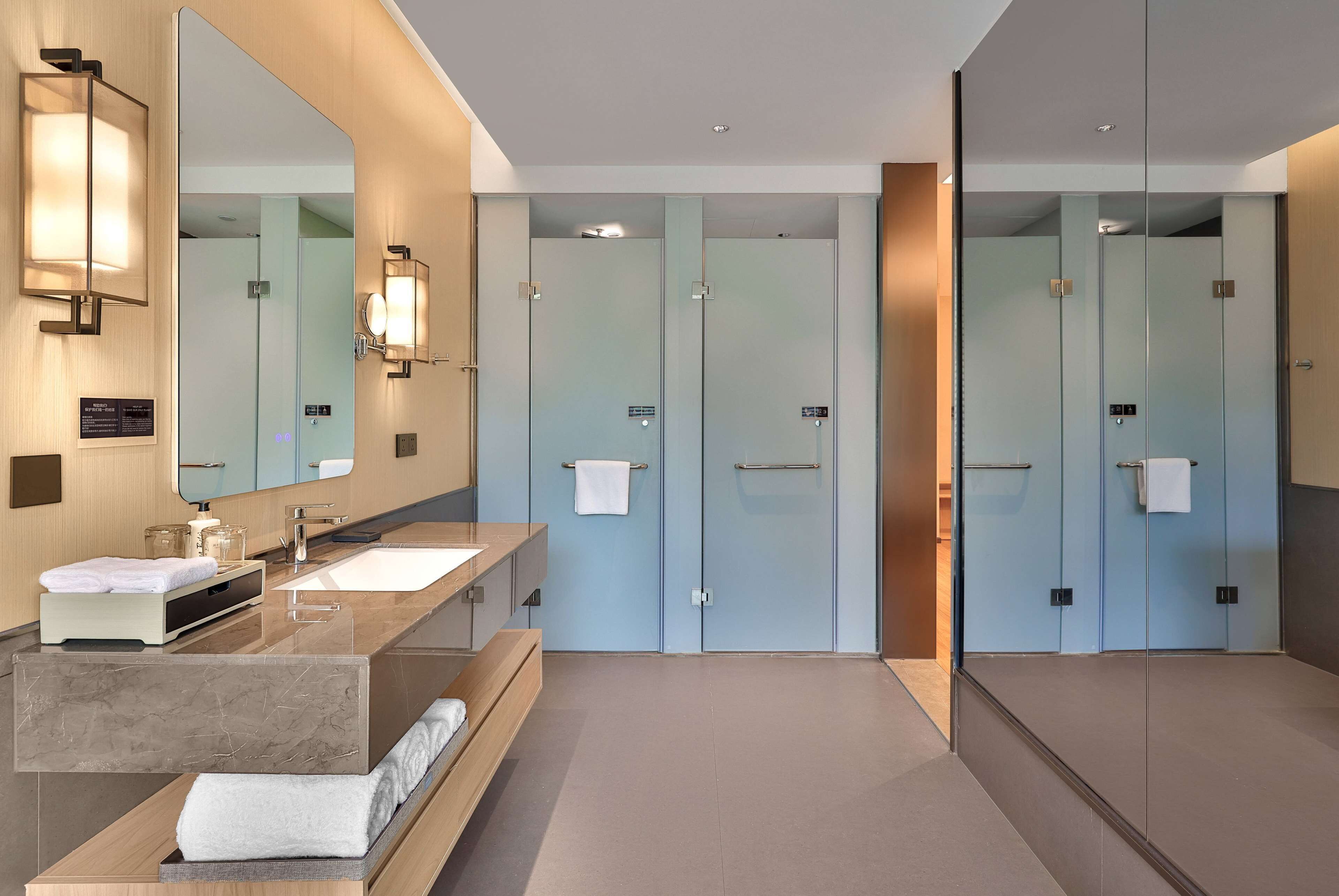 A modern bathroom with a large mirror, two sinks, a vanity, and a glass-enclosed shower area.
